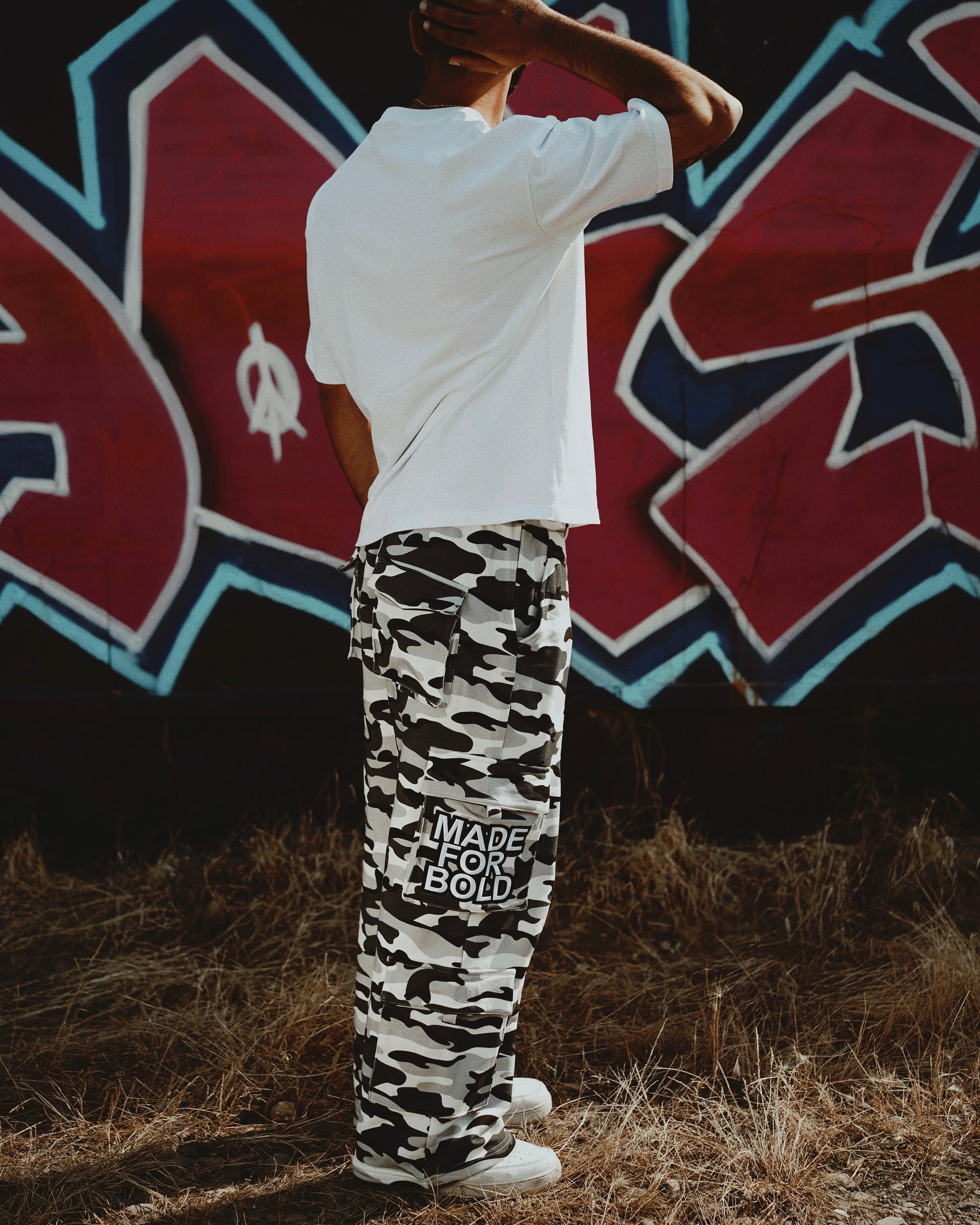 wfwh camouflage pants with text, standing in front of a graffiti wall.