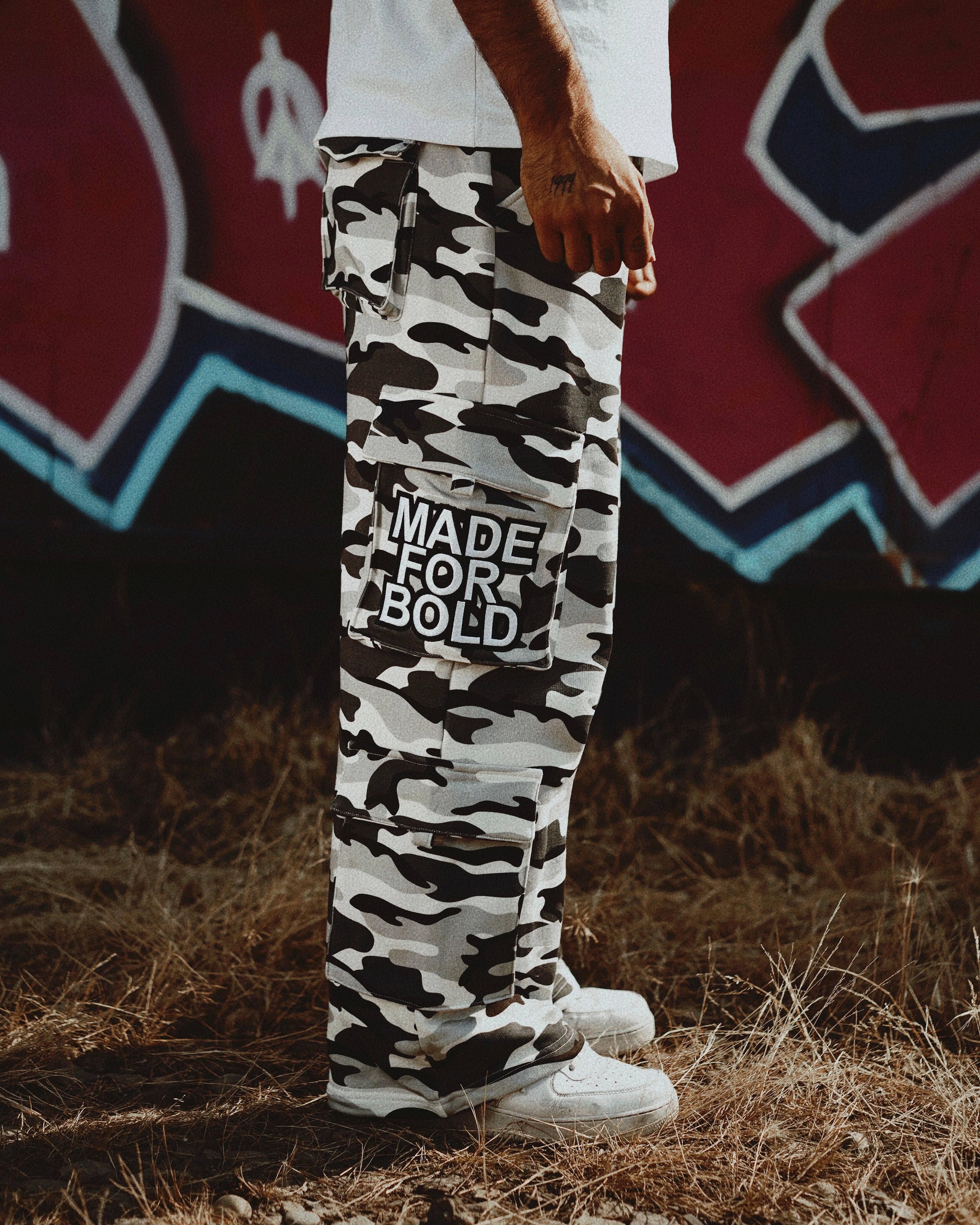 Person wearing camouflage pants with 'Made for Bold' text, standing in front of a graffiti wall.