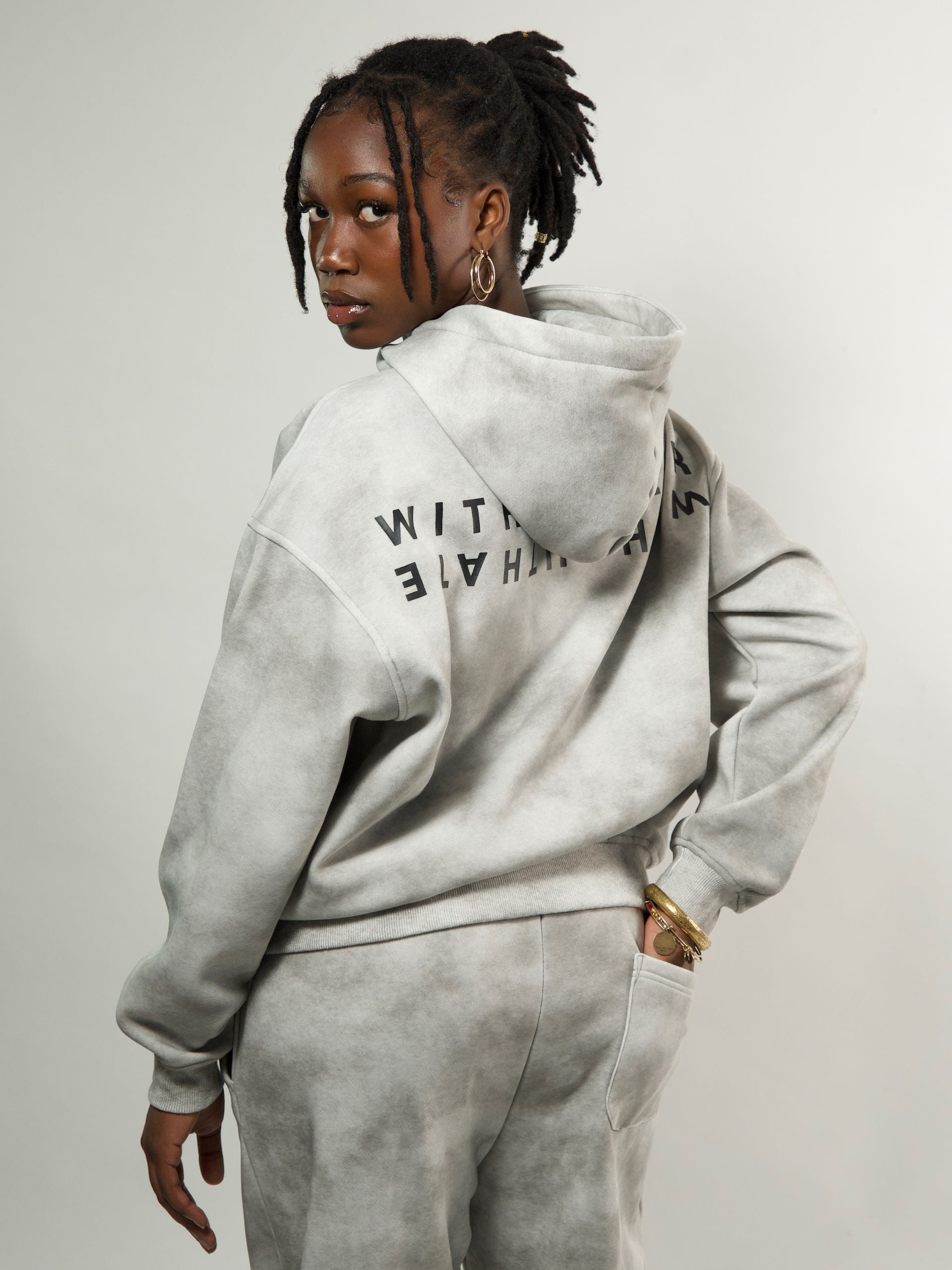 Person wearing a gray hoodie with text on the back against a plain background