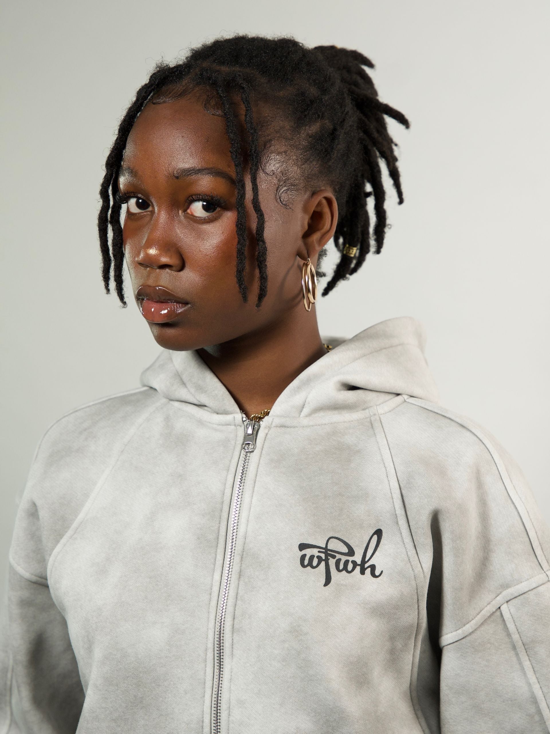 Person wearing a light gray hoodie with a logo on a plain background